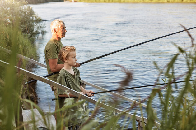 钓鱼欧洲灰白头发的成熟父亲带着儿子在湖边或河边钓鱼 站在水边 手里拿着鱼竿 穿着随意 享受爱好和自然小父亲幼儿