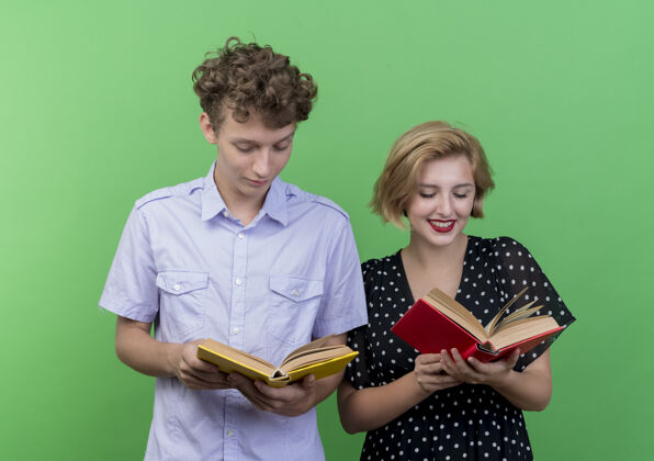 站着一对年轻漂亮的夫妇站在绿色的墙壁上 手拿书本 面带微笑地看着他们脸抱着男人