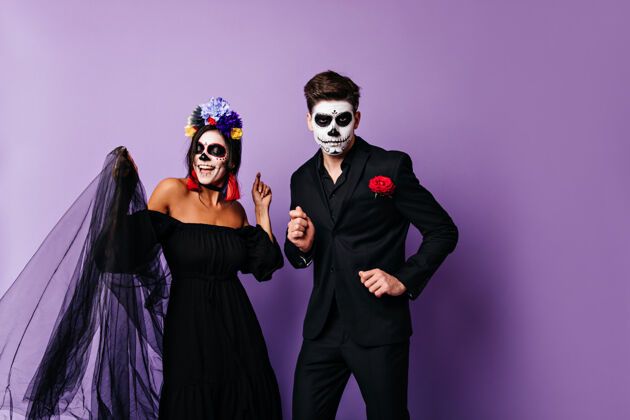 婚礼一个淘气的黑衣女人和她严肃的男朋友在紫色的背景上跳舞一对穿着墨西哥式万圣节服装的情侣的画像花死亡之日恐怖