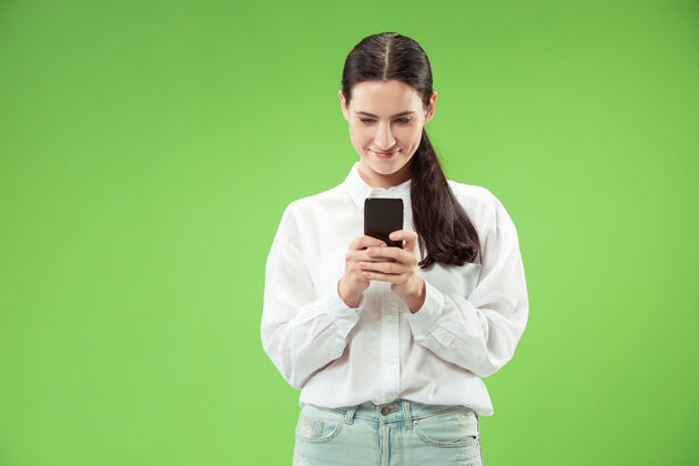 持有年轻漂亮的女人用手机在绿色的墙上人的面部情感概念手机情绪休闲