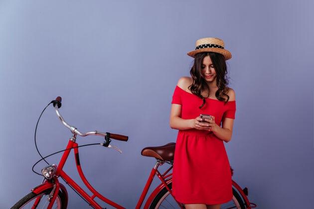 寒冷穿着考究的卷发女孩在紫罗兰色的墙上发短信站在自行车旁看手机屏幕的白种人时尚女人兴奋自行车手自行车