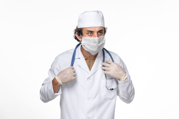 药品正面图：男医生穿着医疗服 戴着口罩 以防白色办公桌上的冠状病毒大流行男性大流行防护