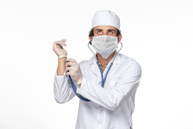 男人正面图：男医生穿着医疗服 戴着口罩以防感染冠状病毒-在白墙冠状病毒大流行药物上检查脉搏大流行医疗专业