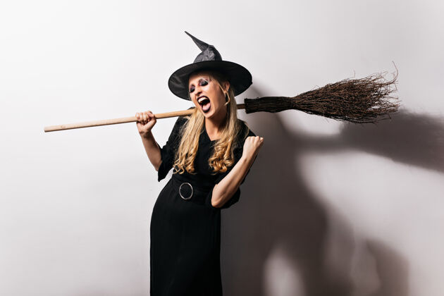 微笑穿着黑色套装的妖娆女巫正在享受派对拿着扫帚的迷人金发巫师庆典邪恶恐惧