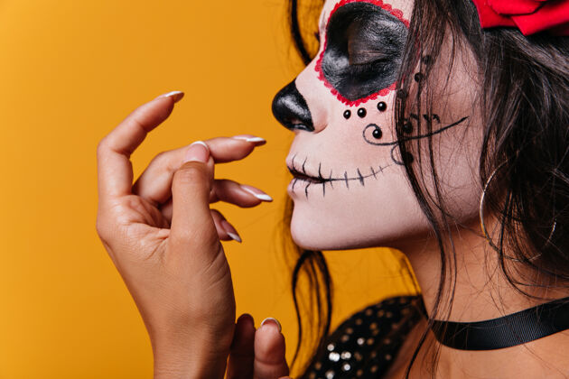 民间传说一个年轻的墨西哥女孩 头上戴着玫瑰 脸上戴着骷髅头 闭着眼睛摆出可爱的姿势化妆恐怖脸