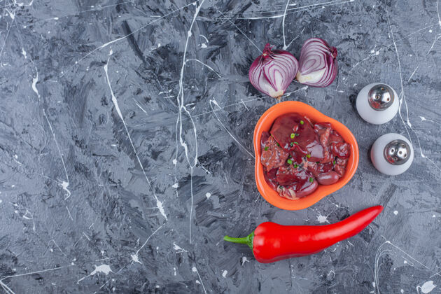开胃菜一碗鸡肝放在洋葱旁边 盐和胡椒放在蓝色的表面上蔬菜碗鸟