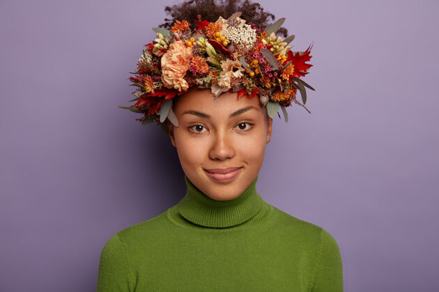 一个自信平和的黑皮肤女模特直视镜头 有着平静快乐的表情 戴着漂亮的手工花环 站在紫色背景下的室内情感黑色秋天