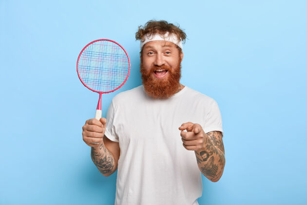 球拍快乐友好的红发网球运动员拿着球拍对着蓝色的墙壁摆姿势运动姜运动员