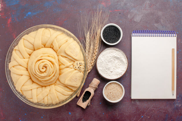 调味品在深紫色的桌子上可以俯瞰用调味品和记事本做成的圆形生馅饼贝壳财务记事本
