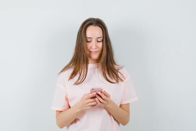 衣着年轻的女士穿着粉红色的t恤 兴高采烈地看着手机 正前方的景色室内电话微笑