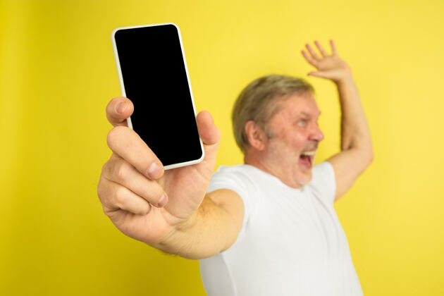 一显示手机的空白屏幕 指向上黄色工作室背景上的白种人肖像穿着白衬衫的漂亮男模手机长度肖像