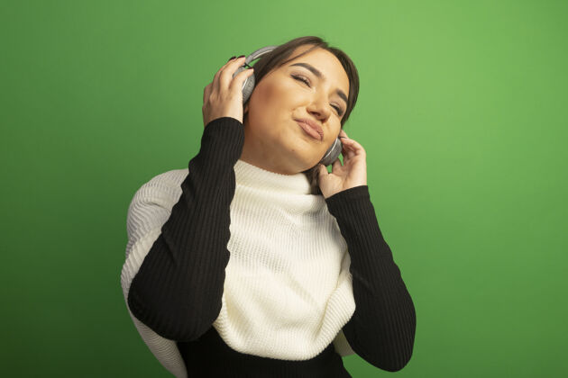 围巾戴着白围巾和耳机的年轻女子正在欣赏她最喜欢的音乐耳机绿色最爱