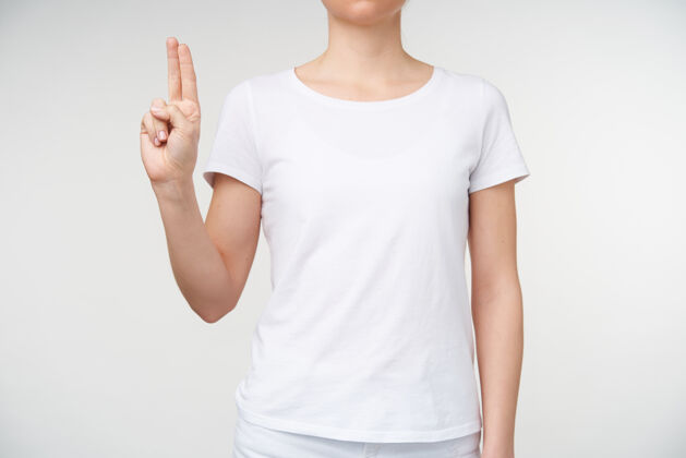 女性年轻女性保持两个手指在一起的水平照片 同时显示字母u使用死亡字母表 隔离在白色背景的休闲服庄稼手势沟通