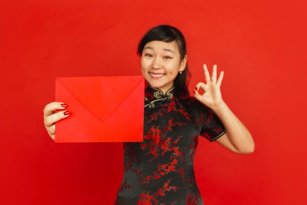 庆祝中国新年红色背景上孤立的亚洲少女肖像身着传统服装的女模特看起来很开心 微笑着 拿着红包庆祝 节日 情感新欢乐祝福