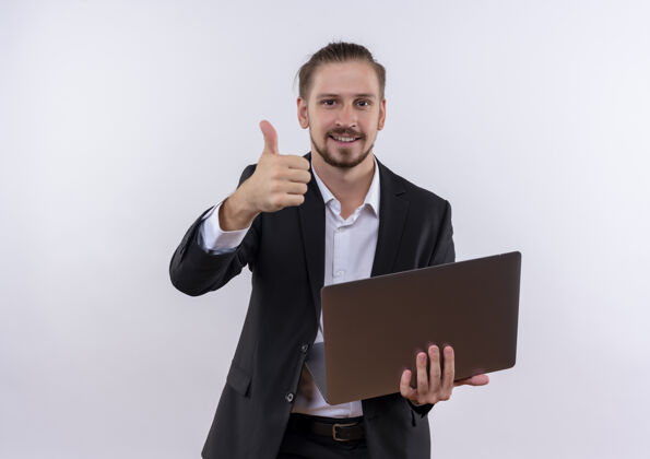 男士穿着西装的帅哥拿着笔记本电脑兴高采烈地笑着竖起大拇指看着站在白色背景上的相机拇指帅气商务