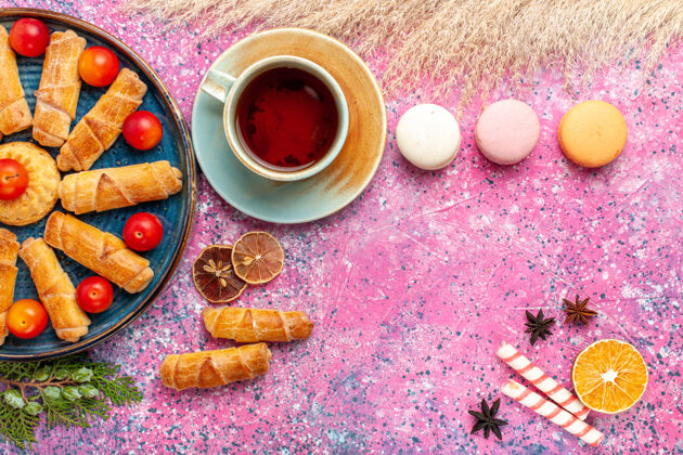 顶部在浅粉色的桌子上 俯瞰甜美美味的百吉饼 新鲜的酸李子 法国马卡龙和一杯茶美味饼干咖啡