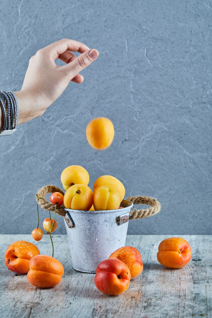 成熟用手把杏子扔进大理石表面的小油桃桶里食物生的营养