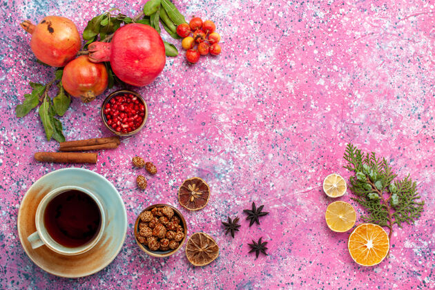 生的顶视图新鲜石榴与绿叶和一杯茶在粉红色的表面食物石榴水果