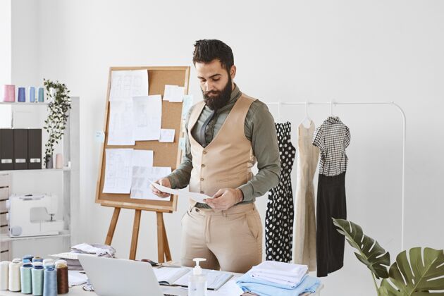 设计师帅气的男时装设计师正拿着报纸在工作室工作服装裁缝电脑