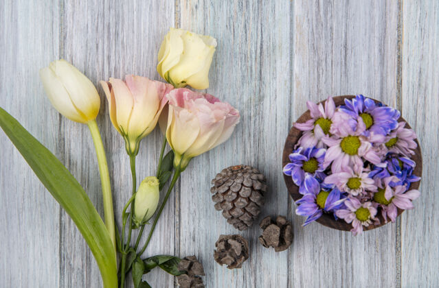 顶顶视图五颜六色可爱的雏菊花在一个木制碗松果和白色郁金香在灰色的木制背景花碗草