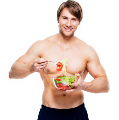 没刮胡子年轻快乐的肌肉男在白墙上吃沙拉胡茬蔬菜健美