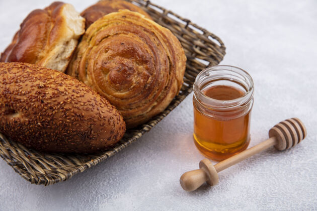 面包顶视图面包桶上蜂蜜的玻璃罐和木制蜂蜜勺上的白色背景罐子桶食物