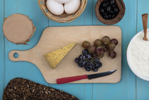 视图俯瞰葡萄与奶酪的立场与橄榄鸡蛋酸奶和黑面包在绿松石背景奶酪黑色橄榄