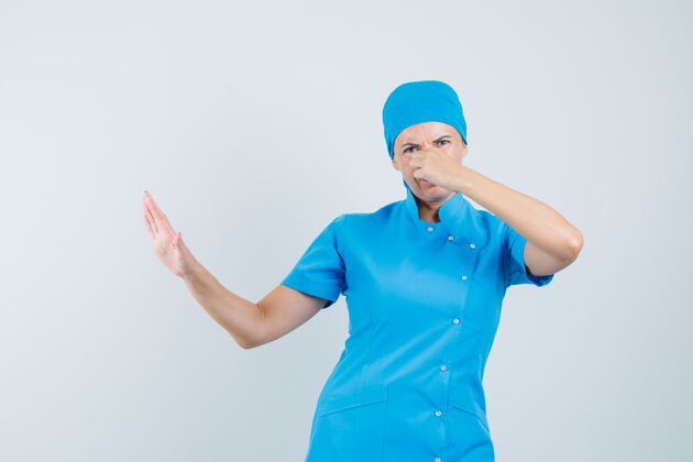年轻人女医生穿着蓝色制服捏鼻子 因气味难闻而显得恶心 前视图气味鼻子治疗