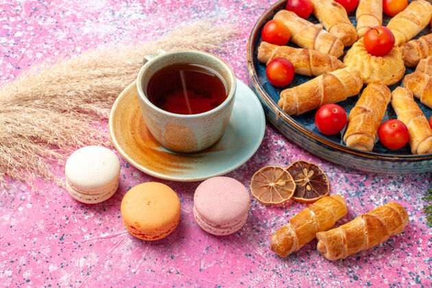 生的在浅粉色的桌子上 可以看到甜美美味的百吉饼 新鲜的酸李子 法国马卡龙和一杯茶派食物饮料