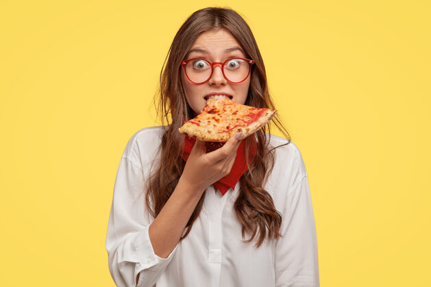 高兴情绪化的美女咬着美味的披萨 直接找时间吃零食 逛披萨店 惊喜低价 模特过黄墙人 快餐和营养披萨店午餐持有