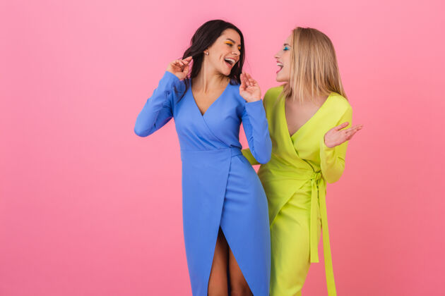 休闲两个时尚的微笑迷人的女人在粉红色的墙上摆着有趣的姿势 穿着蓝色和黄色的时髦多彩的裙子 春天的流行趋势春天女士夏天