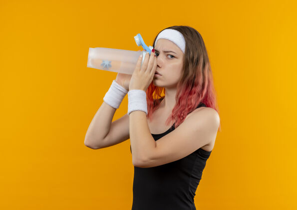 水穿着运动服的年轻健身女 正脸站在橙色的墙上 喝着水年轻运动装市民