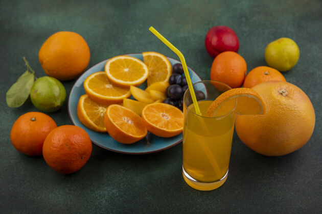 盘子侧视图橘子片和樱桃李子放在蓝色盘子上 橘子汁葡萄柚和柠檬加青柠放在绿色背景上酸橙新鲜食物