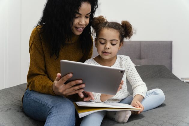 年轻笑脸少女帮妹妹使用平板电脑上网上学姐妹学习教育
