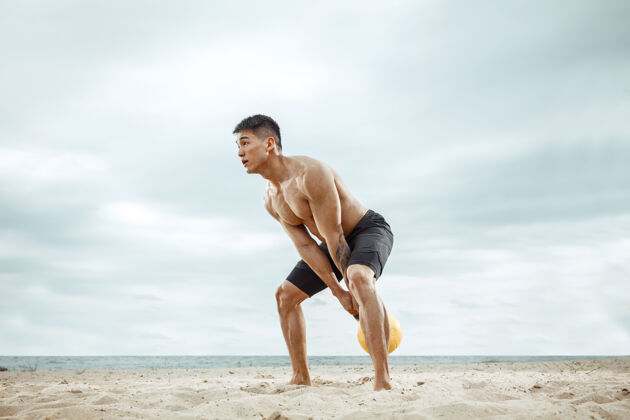 锻炼年轻健康的男子运动员在海滩上做深蹲沙滩健身私人教练
