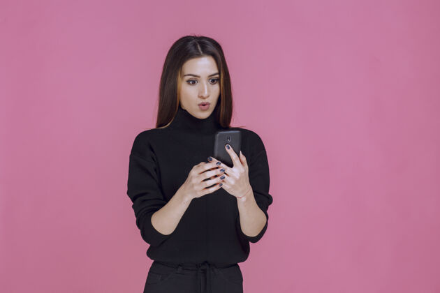 手机穿着黑色毛衣的女人拿着智能手机发短信或查看社交媒体摆姿势休闲聪明