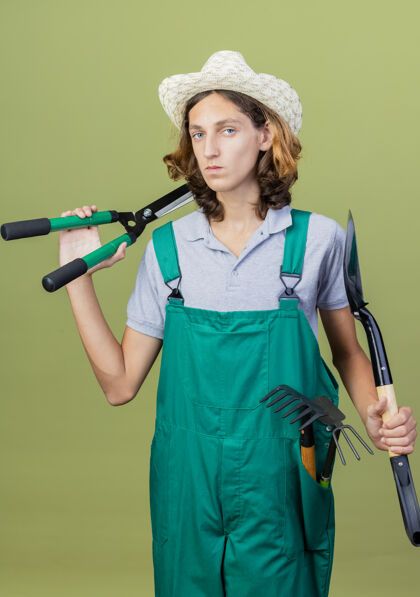 穿年轻的园丁穿着连体衣戴着帽子拿着园艺设备设备花园帽子