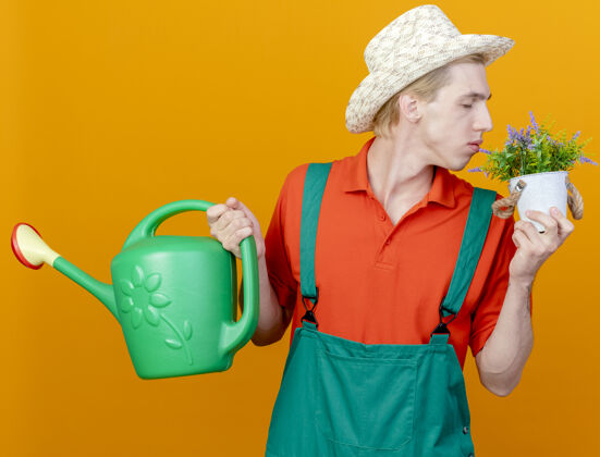 男人年轻的园丁穿着连体衣戴着帽子拿着浇水罐上帝花园感情