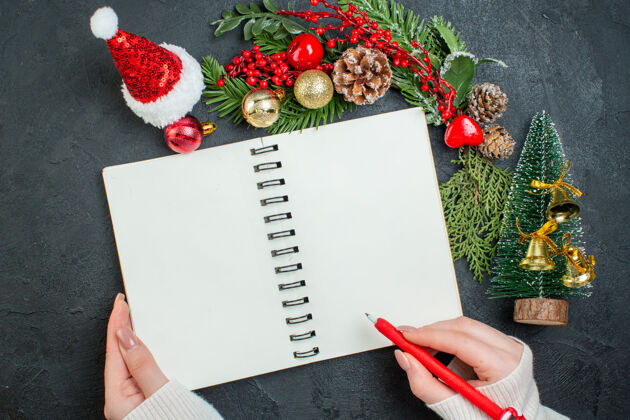 钢笔顶视图圣诞心情与杉木树枝圣诞树圣诞老人帽子手拿一支笔在黑色背景上的螺旋笔记本笔记本螺旋顶部
