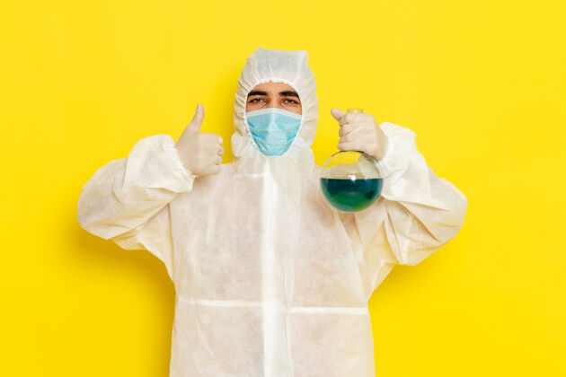 套装身穿特殊防护服的男性科学工作者的正面图 黄色墙上有带面罩的保温瓶科学男性防护