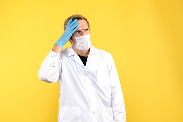 实验室正面图男性医生困惑于黄色背景上的面罩-医疗卫生大流行服装专业人