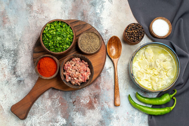 绿色俯视图杜什巴拉一个木制勺子黑色厨房毛巾辣椒碗黑胡椒盐碗肉绿色不同的香料在砧板上裸体表面观点胡椒盐