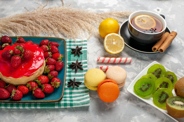 桌子正面是美味的草莓蛋糕和新鲜的草莓 白色桌子上有一杯茶和法式马卡龙美味甜食健康