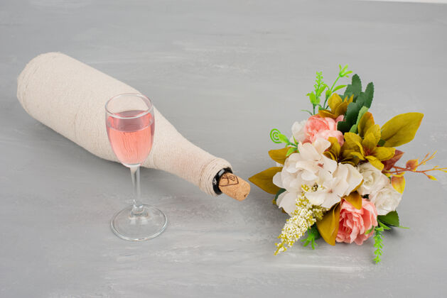 玻璃一束鲜花和一杯玫瑰红葡萄酒在灰色的表面开花花束叶