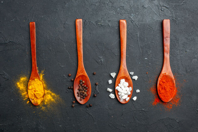 食物顶视图水平排木勺与姜黄黑胡椒盐红胡椒粉放在黑桌子上抹刀旋转特纳