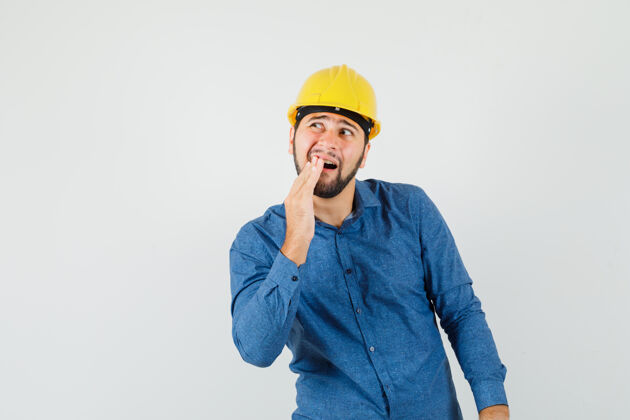 工程师年轻工人穿着衬衫 戴着头盔牙疼 看起来很不舒服制造计算机分析