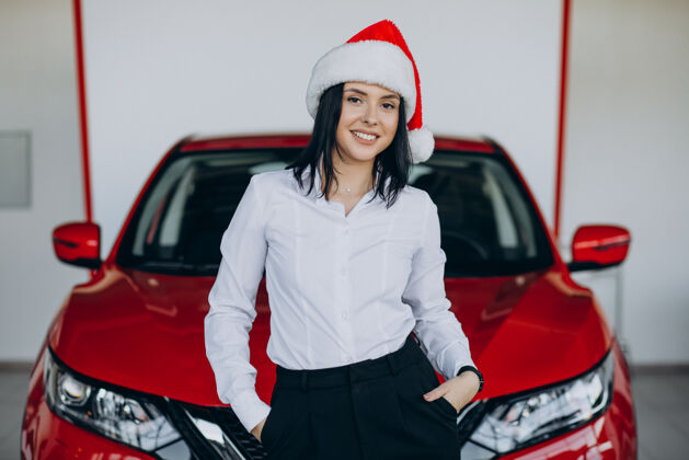 现代一个戴着圣诞帽的女人坐在汽车陈列室里的红色汽车旁边红色女人高兴