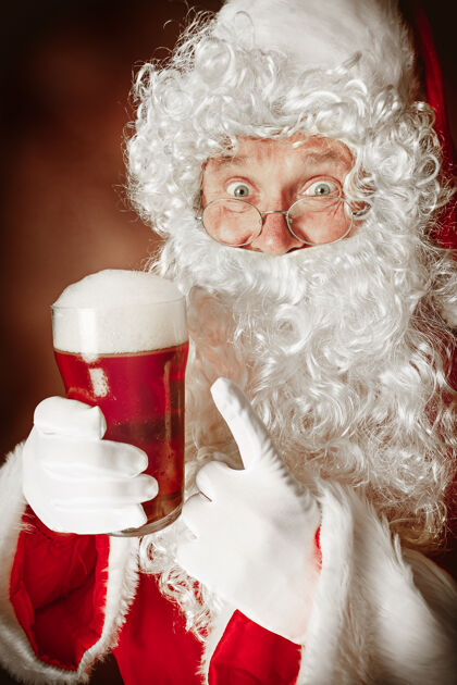 欢乐一个穿着圣诞老人服装 留着奢华的白胡子 戴着圣诞老人的帽子 穿着红色服装的男人的肖像在红啤酒饮料节日胡子