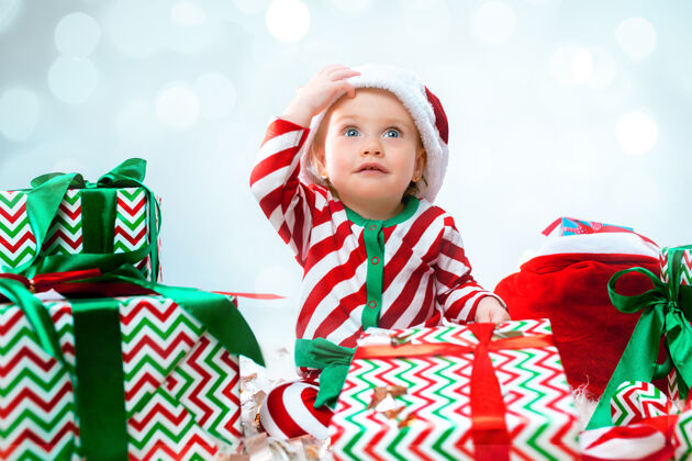 可爱可爱的女婴1岁 戴着圣诞帽 拿着礼物在圣诞装饰上摆姿势拿着圣诞球坐在地板上年轻礼物灯