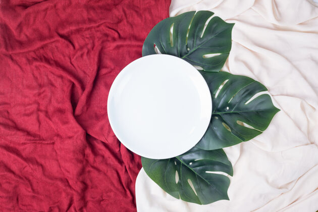 装饰桌布上有人造叶子的白色盘子假的顶视图人造